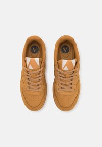 Beige Sneaker aus glattem Wildledermaterial, mit runder Schuhspitze, fünf Ösen und einem kontrastierenden weißen, gemusterten Akzent auf der Zunge.