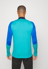 Långärmad träningsskjorta i turkos och blå, med texturerade ärmar med diamantmönster, rund halsringning och figurnära design.