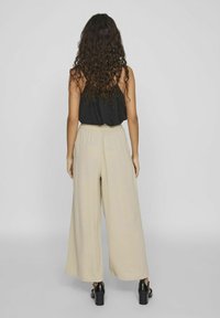 Pantalones de pierna ancha beige con cintura elástica, combinados con una blusa sin mangas negra, vistos desde la parte posterior. Tela suave y corte más holgado.