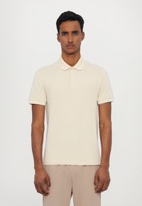 Beige polo tričko s límcem, krátkými rukávy a decentním logem na hrudi. Vyrobeno z hladké tkaniny s designem slim fit.