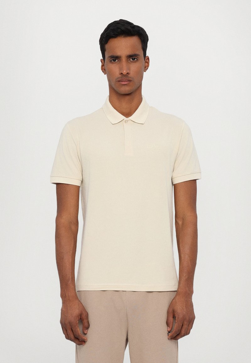 Beige polo tričko s límcem, krátkými rukávy a decentním logem na hrudi. Vyrobeno z hladké tkaniny s designem slim fit.