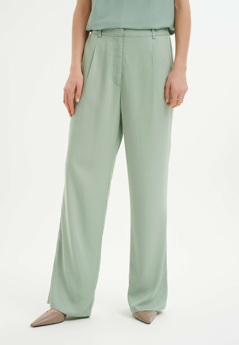 Miętowe szerokie spodnie z lekkiego materiału, z wysokim stanem, fałdami z przodu i bocznymi kieszeniami. Połączone z beżowymi butami na szpilkach.