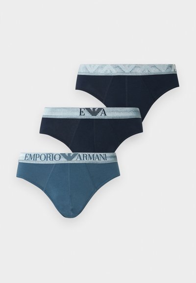 Τρία αντρικά εσώρουχα τύπου briefs σε σκούρες και μπλε αποχρώσεις, το καθένα με γκρι ζώνη μέσης με το λογότυπο και το κείμενο Emporio Armani.