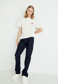 White cotton t-shirt with "LEE" logo, paired with dark blue denim jeans and white sneakers; relaxed fit, short sleeves, smooth texture.