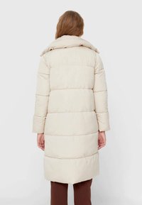 Beige dunjakke med høj krave, quiltet design og lange ærmer. Har en mellemlang pasform og en glat, mat overflade.