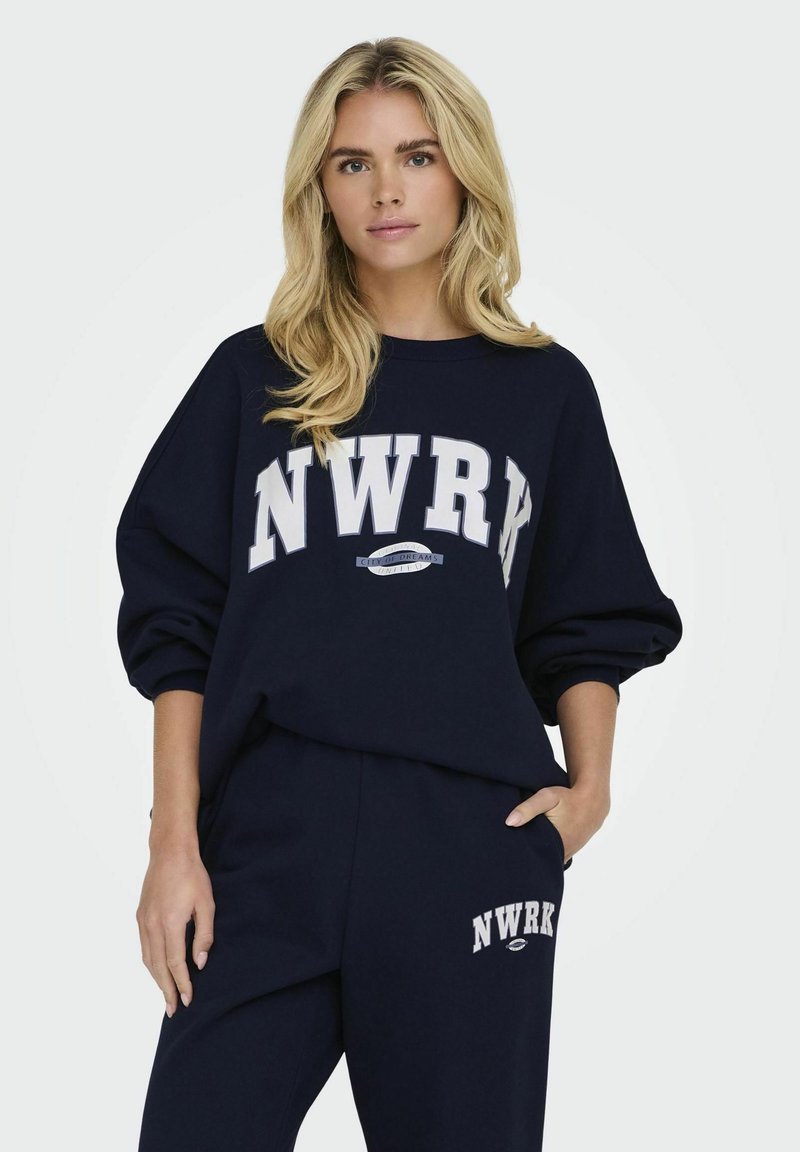 Felpa blu navy con logo "NWRK" in bianco. Vestibilità ampia, polsini a coste, accompagnata da pantaloni della tuta abbinati con un branding simile.