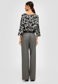 Blouse à imprimé animal noir et gris avec des manches 3/4, assortie à un pantalon large gris taille haute, présentant une texture lisse et des détails soignés.