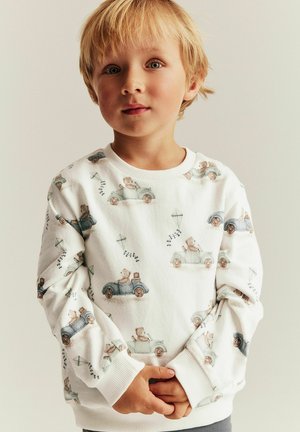 Biała bawełniana bluza z zabawnym nadrukiem niedźwiedzi w samochodach, z jasnoniebieskimi i brązowymi akcentami. Ściągacze na mankietach i kołnierzu.