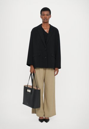 Black oversized blazer with large lapels, beige wide-leg trousers, and a structured black tote bag. Black pointed-toe heels complete the outfit.