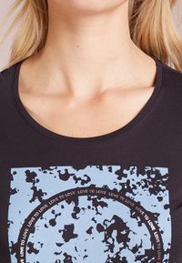 Camiseta negra con un estampado abstracto azul que presenta texto circular. Cuello redondeado y mangas cortas, hecha de una suave mezcla de algodón.