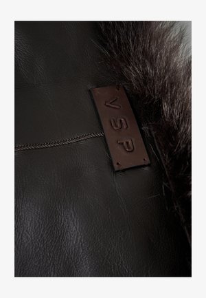 Donkerbruin leer met een gladde textuur, voorzien van een bruin leren label met de opdruk "VSP" en een zachte, bontachtige randaccent.