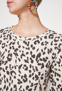 Sweter w panterkę z fakturowanym kremowym tłem i czarnymi plamami. Posiada okrągły dekolt i kolorowe, koralikowe kolczyki w kształcie kół.