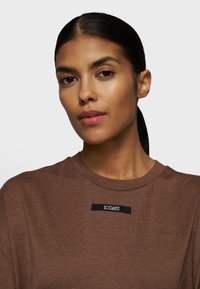 Brun bomulds t-shirt med rund hals og et sort mærke med teksten "10 DAYS" på forsiden. Glat tekstur, afslappet pasform design.