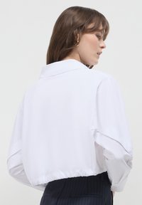 Camicia bianca accorciata con colletto, dotata di un retro con bottoni, vestibilità ampia e orlo elasticizzato. Realizzata in tessuto leggero e morbido.