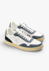 Weiße Sneakers mit blauen Wildlederakzenten, durchlöchtem Zehenbereich, flachen Schnürsenkeln und einer cremefarbenen Sohle. Enthält ein Logo an der Seite und einen kontrastierenden Absatz.