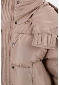 Beige pufferjack met een glanzende, gladde textuur. Beschikt over stikdetails en drukknoopsluitingen. Ritszakken aan de zijkanten.