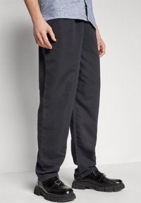 Sorte bukser laget av glatt stoff, med en avslappet passform. Kombinert med glinsende svarte loafers med tykke såler og en metallisk detalj.