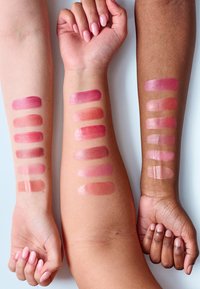 Tres brazos con muestras de colores de labios en tonos variados de rosa y nude, mostrando acabados mate y brillante en tonos de piel claros y oscuros.