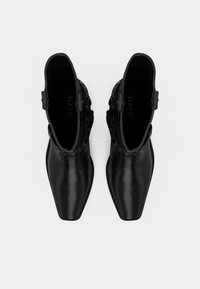 Μαύρα μποτάκια αστραγάλου από λείο δέρμα, με μυτερή μύτη, διακοσμητικά μεταλλικά στοιχεία γύρω από τον αστράγαλο και επίπεδη σόλα.