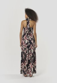 Vestido largo con diseño de cuello halter, tela negra con un patrón tropical en rojo y blanco, y corsé ajustado con falda fluida.