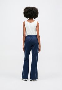 Granatowe spodnie dresowe z białymi paskami po bokach i elastycznym pasem, zestawione z jasnym topem bez rękawów. Gładka tekstura materiału.