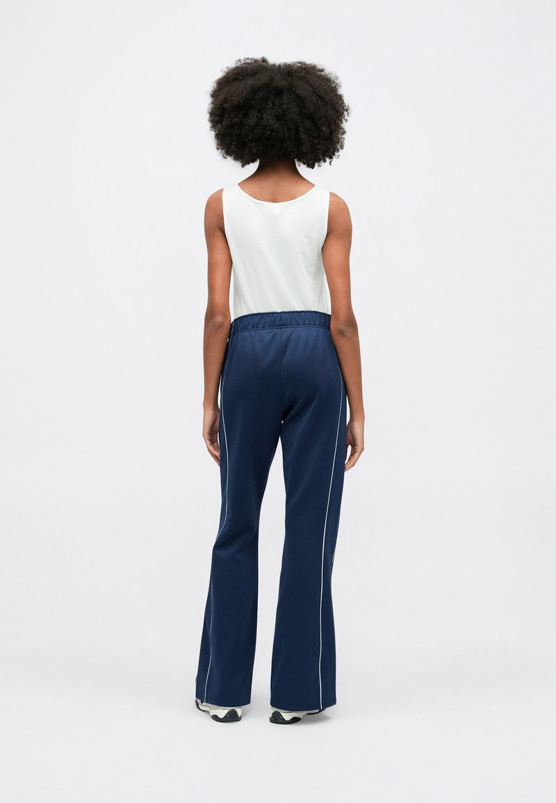 Pantaloni della tuta blu scuro con strisce bianche e una cintura elastica, abbinati a una maglietta senza maniche di colore chiaro. Tessuto dalla texture liscia.