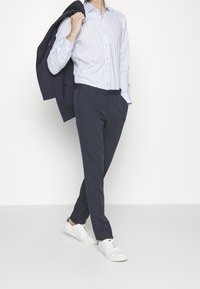 Jasnoniebieska koszula w paski, granatowe spodnie i białe trampki. Koszula ma kołnierzyk na guziki i długie rękawy. Marynarka garniturowa jest granatowa.