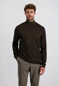 Brauner Rollkragenpullover aus gestricktem Stoff mit glatter Textur. Er hat ein tailliertes Design und lange Ärmel und wird mit grauen Hosen kombiniert.