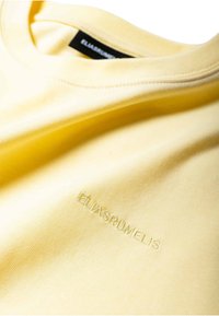 T-shirt en coton jaune à la texture lisse, doté d'un col côtelé et d'une broderie de la marque sur le bas devant.