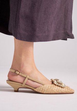 Zapato tipo slingback tejido en color beige con tacón bajo y joya decorativa en la parte frontal, combinado con pantalones anchos de pierna ancha y corte cropped en color púrpura.