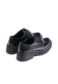 Zapatos de cuero negro con cordones y un acabado suave, que cuentan con una suela de goma gruesa y costuras sutiles. Vista lateral que resalta la forma del zapato.