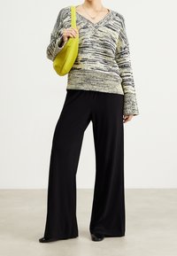 Pull surdimensionné, rayé dans des teintes de vert et de noir ; associé à un pantalon large noir et un sac jaune vif. Texture lisse et coupe décontractée.
