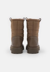 Bottes chevilles marron avec une tige en tissu matelassé et un bas en cuir texturé. Elles possèdent des languettes de tirage doubles et des semelles en caoutchouc robustes pour une meilleure traction.