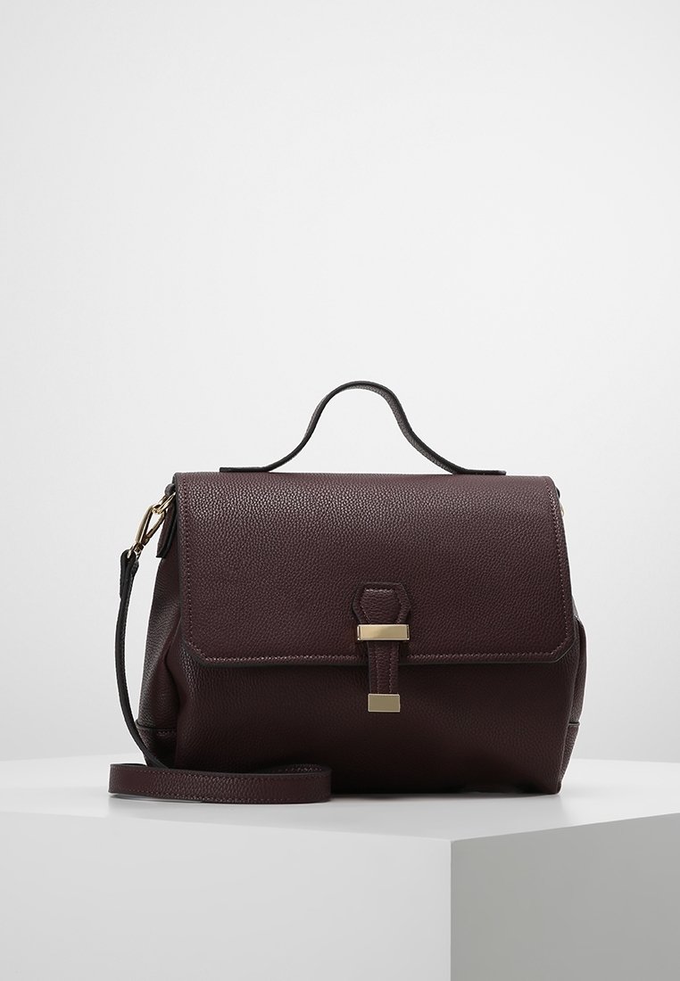 Sac à main en cuir bordeaux avec une surface texturée, une anse supérieure et une bandoulière amovible, dotée d'un détail de fermoir en ton doré à l'avant.