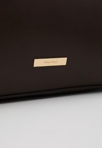 Gros plan sur une surface en cuir marron foncé avec une petite plaque métallique dorée gravée "ANNA FIELD".