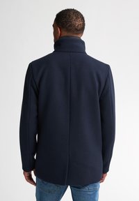 Navyblauer Wollmischmantel mit hohem Kragen, geradem Schnitt und einer mittigen Naht auf der Rückseite. Der Stoff wirkt weich mit einer glatten Textur.