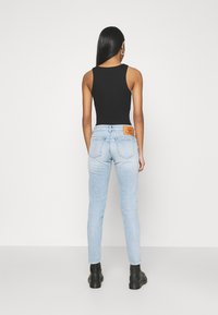 Svart ärmlös topp i kombination med ljusblå smala jeans. Notabla detaljer inkluderar en läderlapp på jeansens baksida och svarta ankelskor.