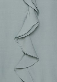 Tissu bleu clair présentant un bord à volants avec une texture lisse et des détails de couture. Le volant s'incurve gracieusement le long du matériau.