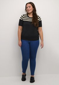 Black and ivory striped short-sleeve knit top with a fitted shape, paired with blue skinny jeans and black glossy loafers. Smooth texture.