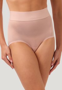 Primo piano di una persona con indosso biancheria intima color carne a vita alta, senza cuciture, realizzata in tessuto liscio e dotata di una fascia larga in vita.