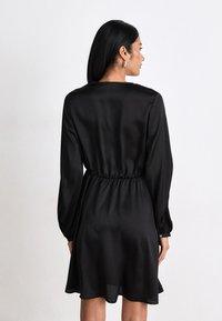 Black, long-sleeved dress with a cinched waist, flared hem, and smooth satin texture, viewed from the back.