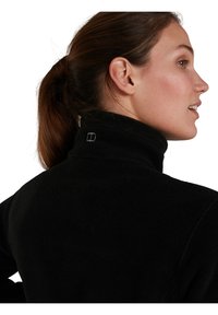 Veste en polaire noire avec un col montant, dotée d'un petit logo dans le dos. Texture douce et coupe régulière.