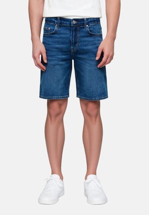 Shorts vaqueros en azul oscuro con un corte recto, cinco bolsillos y detalles de costuras claras. Combinados con zapatillas blancas.