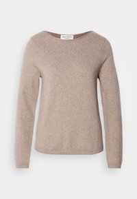 Pull beige à manches longues avec col rond en tissu tricoté doux, présenté à plat avec une étiquette de marque visible à l'intérieur de l'encolure.