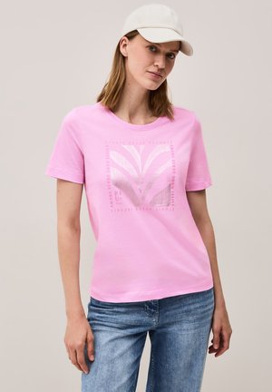 T-shirt en coton rose à manches courtes, col rond, présentant un design graphique métallique et du texte à l'avant, associé à un jean bleu clair.