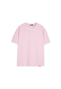 Jasnoróżowa bawełniana koszulka z krótkim rękawem, okrągłym dekoltem i małą różową metką u dołu po lewej stronie. Miękka w dotyku, luźny krój.
