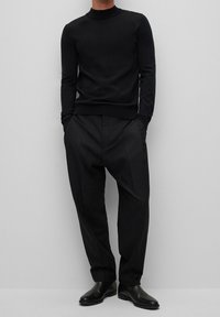 Schwarzer, gerippter Rollkragenpullover kombiniert mit schwarzen, plissierten Hosen, mit einer lockeren Passform und eleganten schwarzen Leder-Stiefeletten.