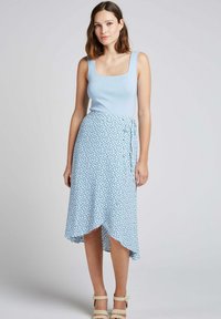 Un débardeur en tricot bleu clair avec un décolleté carré associé à une jupe portefeuille bleu clair présentant un motif floral et un ourlet asymétrique.