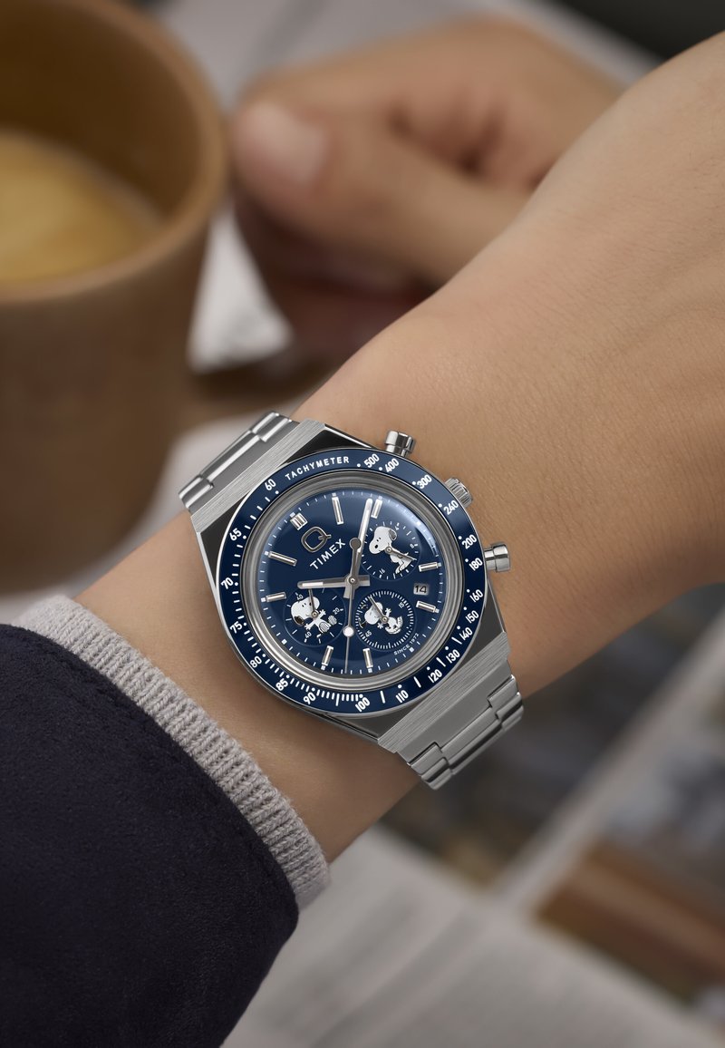 Orologio cronografo in acciaio inox con quadrante blu, accenti argentati, scala tachimetrica e sottodial. Indossato su un polso con una manica grigia.