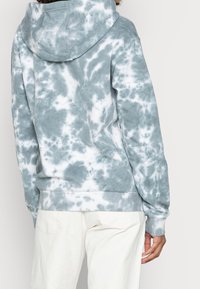 Jasnoszara i biała bluza typu tie-dye wykonana z miękkiego materiału, z kapturem, długimi rękawami oraz ściągaczami na dolnym brzegu i mankietach. Teksturowany, casualowy design.